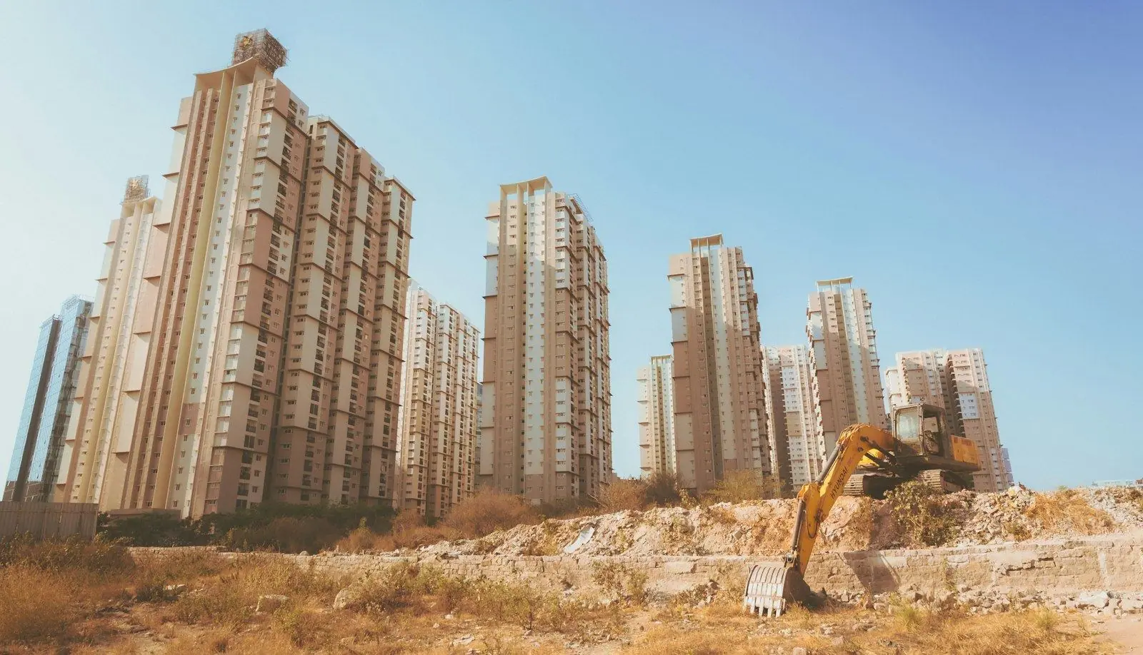 Excavator working on open ground in front of new apartment towers